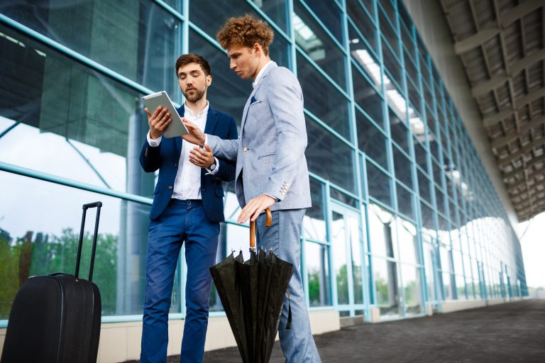 Picture of two young businessmen talking on airport background and holding tablet