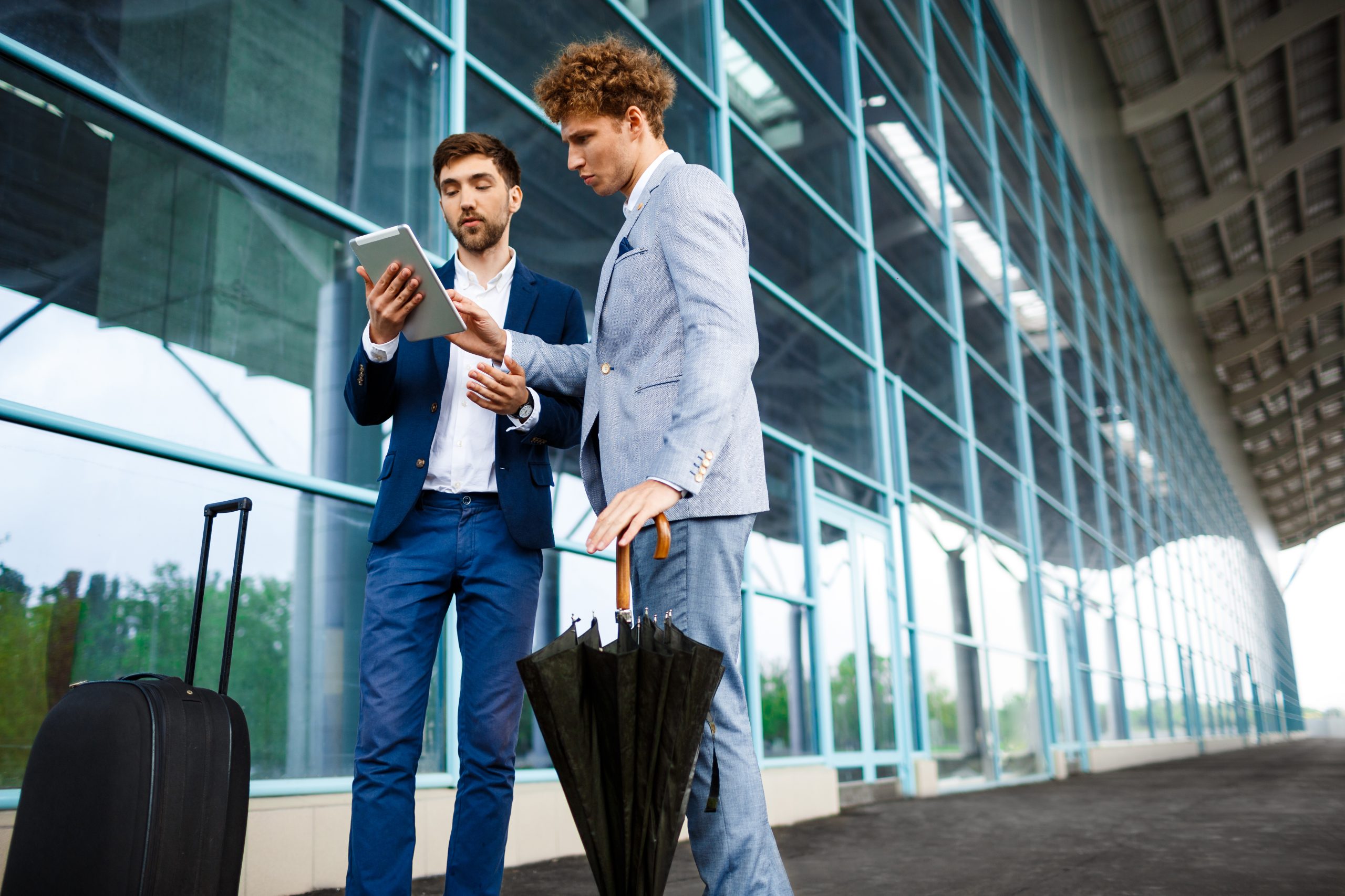Picture of two young businessmen talking on airport background and holding tablet